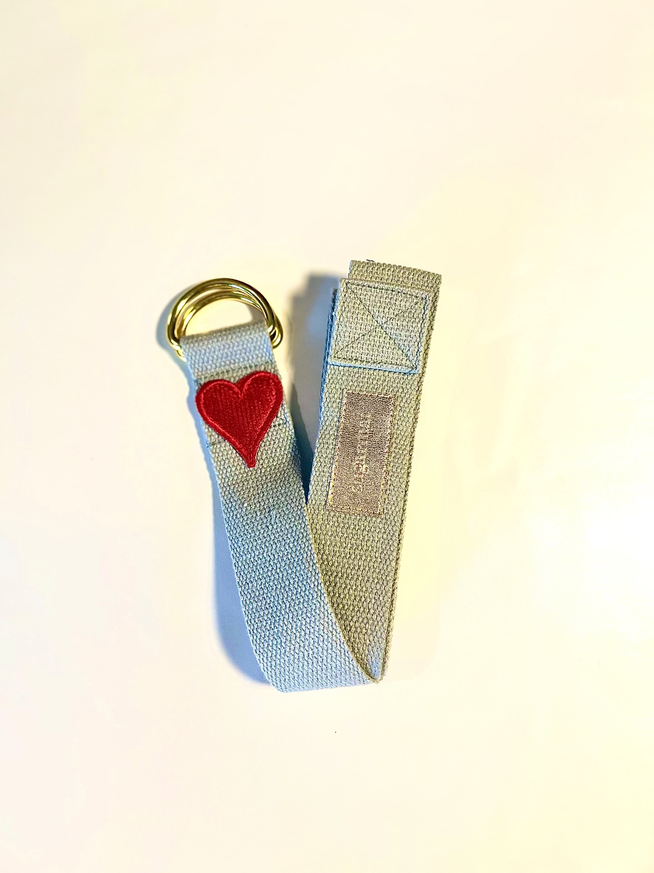Light blue strap with red heart and gold ring on a beige background