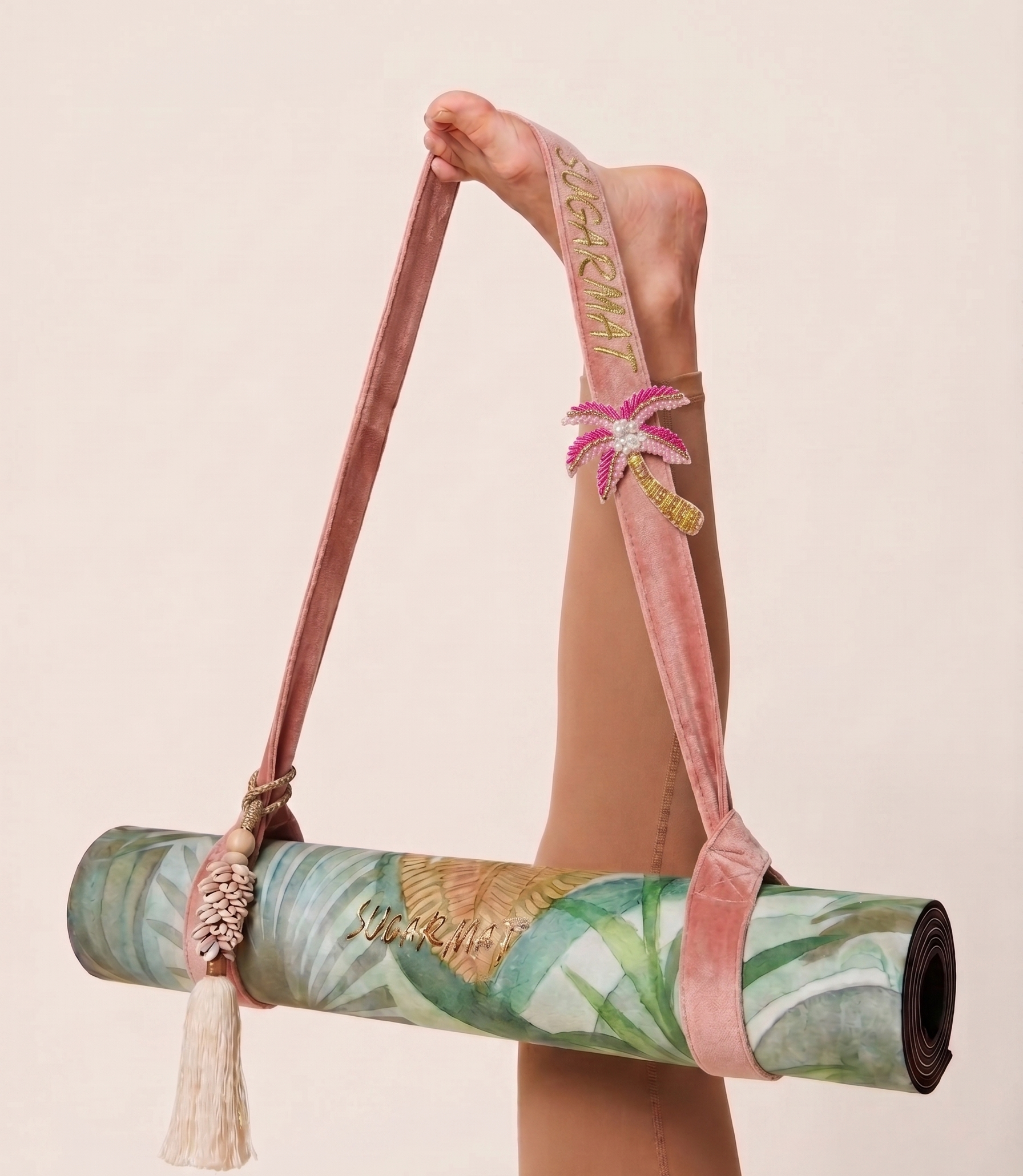 Yoga mat with floral design held by a strap with palm tree design on a beige background