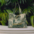 Tropical leaf-patterned bag on a white surface with green foliage in the background