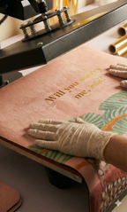 Person wearing a glove applying pressure to a leather product with text and graphics.
