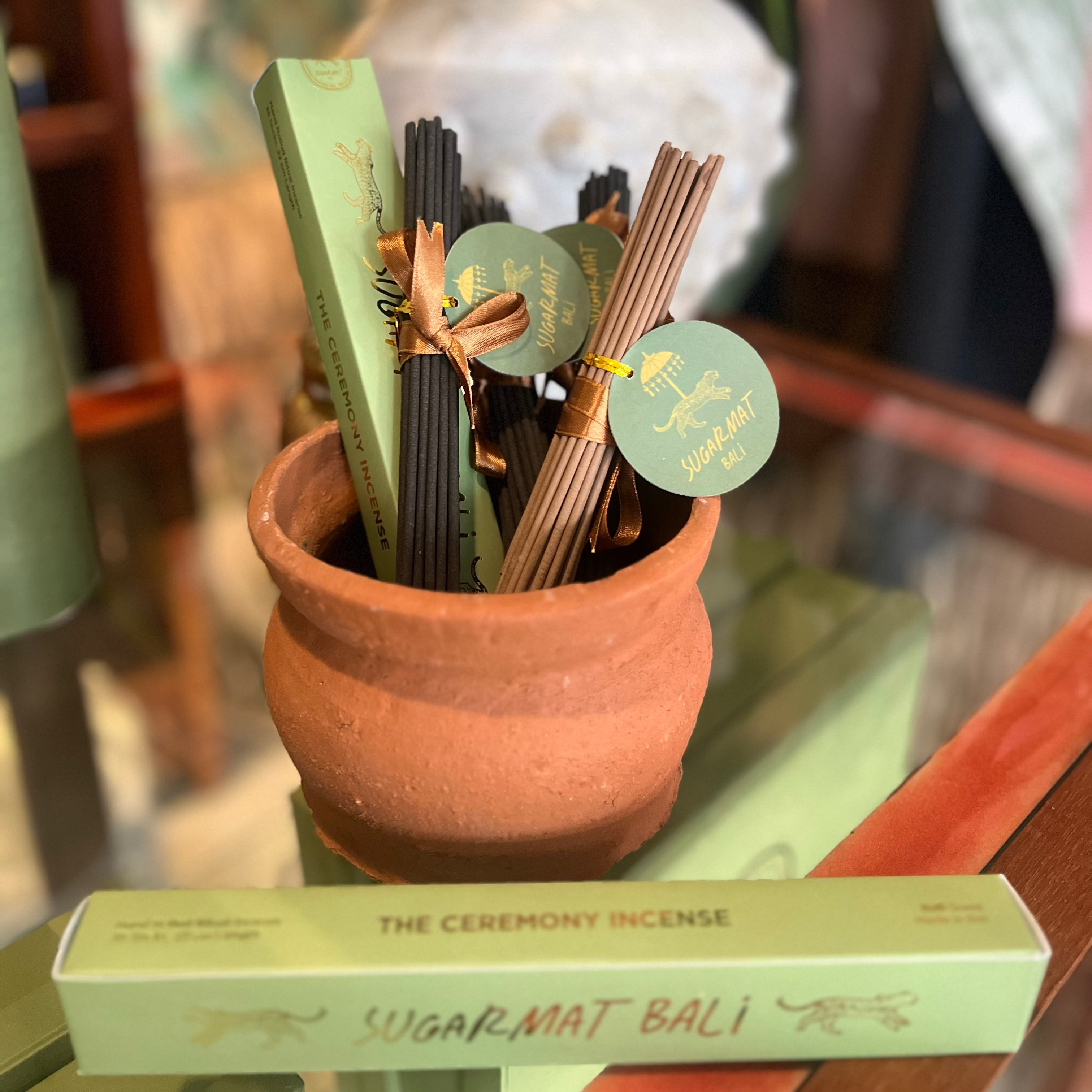 Incense sticks in a terracotta pot with green labels on a glass surface, surrounded by plants.